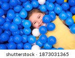 Small photo of girl in multi-colored ball in children's playgroup. the child smiles, hiding in the balls