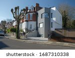 Small photo of London/ UK - MARCH 24th 2020: Boy jumping off wall in front of incongruous modern house extension on Highgate street.