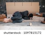 Small photo of Helpless and defenceless man is lying on the cardboard on concrete floor and sleeping. He is covering his face with hands hiding it from the sun. There is a sign besides him says homeless please help.