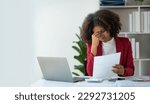 Small photo of Young african american businesswoman reading document with misinformation Unrealistic financial data, feeling stressed and nervous while sitting on laptop at desk in office.