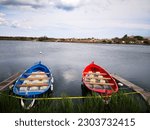 Small photo of Two colorful runabout pleasure boats painted in red and blue with wooden seats inside moored to wooden berth in small inlet of Mediterranean sea, with green grass in foreground and blue sea water