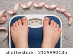 Small photo of Women's bare feet on floor scales and measuring tape, weight 100-110 kilograms, top view. The idea of obesity, weight loss and excess weight.