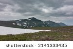 Small photo of In a high-altitude valley there is melted snow. There is scant vegetation on the rocky soil. A picturesque mountain range against a cloudy sky. Kamchatka
