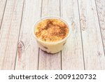 Individual tiramisu dessert with cinnamon and powdered chocolate inside a home delivery container on wooden table