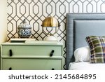 Small photo of Bedroom with double bed with upholstered headboard with studs and gray fabric, pale green wooden bedside table, metal lampshade lamp and wallpapered walls