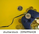 Crypto gaming. Play for earn concept. Top view of a video game controller joystick with focus on a bitcoin cryptocurrency coin on top,  gold coins underneath. Copy space. Vivid yellow background.