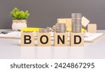 Small photo of the concept conveyed by the image of wooden blocks spelling BOND with a stack of coins above symbolizes financial financial security, investment opportunities, and wealth accumulation through bonds