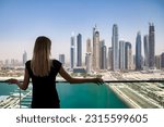 Small photo of Rear view of young cute woman in black on balcony with view of skyscrapers Dubai UAE, pensive looking. Lovely lady posing from behind on terrace of tower block. Leisure activity concept. Copy ad space