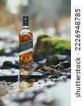 Small photo of Krasnoyarsk, Russia - 11.15.2022 A bottle of Johnny Walker Green Label Scotch Whiskey stands on a rock in the creek. Autumn landscape with snow.