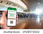 The digital green pass of the european union with the QR code on the screen of a mobile held by a hand with blurred airport in the background. Immunity from Covid-19. Travel without restrictions.