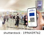 EU Digital COVID Certificate with the QR code on the screen of a mobile held by a hand with blurred airport in the background. Immunity from Covid-19. Travel without restrictions.