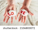 Small photo of Hands of little girl hold two white smooth stones with syllables lo and ve painted red on white cloth background. Family, love, holidays, birthday, Valentine's day, Mother's day concept. Copy space.