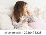 Small photo of Poor, unfortunate little brunette preschooler child, girl in pajamas coughing, lying in soft bed. Sore throat, angina, tonsillitis. Recovering, health care, home treatment and bed rest. Copy space