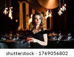 Beautiful blonde, young girl holding an aperol spritz. Cocktail aperol spritz in a glass. Portrait of a young girl in a restaurant. Portrait of a girl. Young girl in a restaurant with a glass.