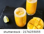 Mango and lime juice nectar. A refreshing summer drink on a black background. Bright yellow and black colors. Mango juice on a dark background. Summer drink with ice and slices of mango and lime.