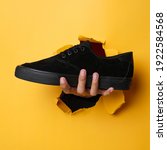 Small photo of Plain black sneakers with a purple base. Plimsoll shoes on a yellow background give a bright effect to the photo. Front shot. Side shot. Hands holding sneakers through yellow paper background.