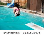 Young brunette jumping off a diving board into an outdoor swimming pool. Woman in black and pink bikini doing caught in mid air doing a cannon ball into a private swimming pool in the backyard.