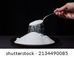 Small photo of Salt is poured from a spoon onto a plate with salt on a black background. Excessive salt intake. Coarse Rock salt