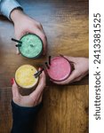 Small photo of "Smoothies in three different colors, held in three hands: yellow smoothie, green smoothie, pink smoothie.