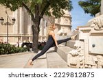 Middle-aged blonde woman, wearing a black bodysuit, doing leg stretching exercises for meditation and yoga on the stairs of the city. Concept yoga, meditation, concentration, sport, mindfulness.