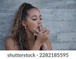 Small photo of Latina and Hispanic girl, young and nonconformist, rebellious, lighting a cigarette rolled by herself, on a gray background. Concept tobacco, smoke, fire, addiction, gangs.