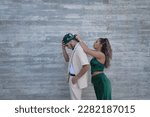 Small photo of Latin and Hispanic boy and girl couple, young and nonconformist, where she ties his headscarf from behind, on a gray cement background. Concept love, couples, lovers, valentine's day.