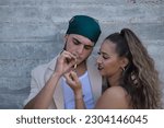 Small photo of Latino and Hispanic boy and girl couple, young and nonconformist, rebellious, hugging while she lights a cigarette for him. Concept tobacco, smoke, fire, addiction, gangs, couples.