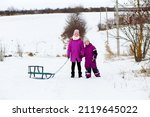 Small photo of Two funny little girls having fun with a sleight in beautiful winter park. Cute children playing in a snow. Winter activities for kids.
