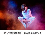 Small photo of Blooming. Teen girl in fencing costume with sword in hand isolated on black background, neon lighted smoke. Practicing and training in motion, action. Copyspace. Sport, youth, healthy lifestyle.