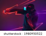 Young African man playing with VR set isolated on dark purple studio background in neon light with geometric luminescent shapes, stripes. Motion, action, youth culture, modern technology concept.
