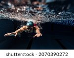 Small photo of Dark blue water, depth. Underwater view of swimming movements details. One female swimmer in swimming cap and goggles training at pool. Healthy lifestyle, power, energy, sports movement concept.