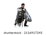 Small photo of Make fealty. Portrait of serious manm medieval warrior, knight in armor sitting on one knee isolated over white background. Knight's noble oath. Comparison of eras, history, renaissance style