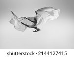 Small photo of Like soaring angel. Black and white portrait of graceful ballerina dancing with fabric, cloth isolated on grey studio background. Grace, art, beauty, contemp dance concept. Weightless, flexible