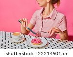 Young woman having delicious breakfast with donut and coffee over pink background. Yummy. Vintage, retro style interior. Food pop art photography. Complementary colors. Copy space for ad, text