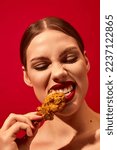 Small photo of Young woman with red lipstick eating fried chicken, nuggets over vivid red background. Fast food lover. Food pop art photography. Complementary colors. Junk food. Copy space for ad, text