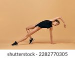 Flexible athletic young girl in black bodysuit training against orange studio background. Workout session. Concept of sport, healthy and active lifestyle, beauty, fitness. Copyspace for ad