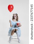Small photo of Conceptual image of young girl wearing Halloween dress of dancing clown with spooky make-up isolated on grey background. Concept of holiday, party, creativity, ad and traditions. Scare night