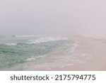 Teal colored waves crashing up on the foggy misty Pensacola Florida beach.	