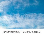Cirrus clouds and long airplane trail row. Aero plane contrail in blue cloudy sky background. Horizontal line track from flying fast aeroplane in distance
