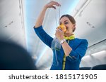 Portrait of smiling cheerful flight attendant demonstrating how grasping mask over nose and mouth while slip elastic band over head