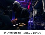 Hacker seated in server room launching cyberattack on laptop
