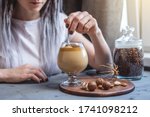 A woman uses a spoon to stir the whipped mousse from Dalgona coffee in a clear cup. Delicious cold drink. Trendy spectacular drink that can be prepared at home