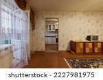 Example of Old Soviet Russian poor interior in Khruschev House. Aged sideboard, tv set, curtains, kitchen furniture. Shabby floor. Tattered wallpaper on wall. Carpet as decor. Apartment of pensioners.