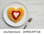 Heart shaped spaghetti with tomato sauce and parmesan cheeses on white plate with white wood background.Romantic vegetarian art food idea for Valentine's dinner.Top view.Copy space