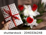 white gift envelope with red ribbons in white paper for certificates, invitation card inside into woman's hand. Craft concept. Weddig, ceremony concept, holidays, surprises. Blurred flowers background
