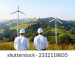 sustainability and net zero concept, two engineer standing in a field with wind turbines in the background and a hill.