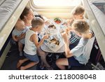 Family of mother holding baby and sons sitting at table and having lunch in train car with bunk beds against bright sunlight