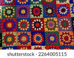 Small photo of Beautiful multi-colored plaid, knitted from squares. The squares are crocheted with red, yellow, green, purple, blue and orange yarn. Blue and yellow colors predominate. Granny square.