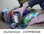 Small photo of Donation cardboard box with various food (pasta, rice, oil, tuna, canned goods...) and a man's hands adding a chickpeas can..