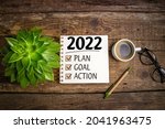 New year goals 2022 on desk. 2022 resolutions list with notebook, coffee cup and eyeglasses on wooden background. Goals, plan, strategy, business, idea, action concept. Top view